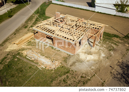 Aerial view of unfinished brick house with wooden roof frame structure under construction. 74737802