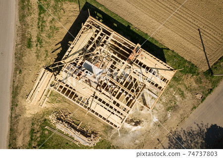 Aerial view of unfinished brick house with wooden roof frame structure under construction. 74737803