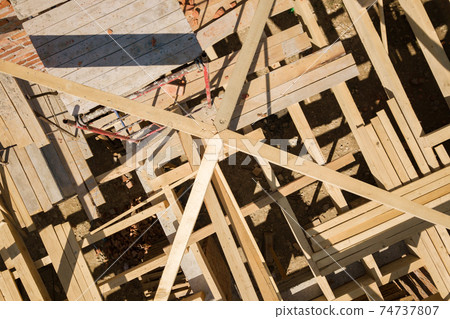 Aerial view of unfinished brick house with wooden roof frame structure under construction. 74737807