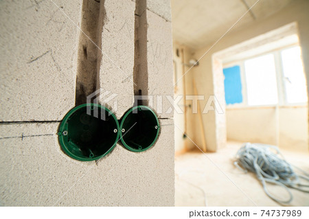 New electrical wiring installation, plastic boxes for electrical cables for future outlet sockets on the wall, renovation concept. New electrical wiring installation, plastic boxes for electrical cables for future outlet sockets on the wall, renovation concept. 74737989