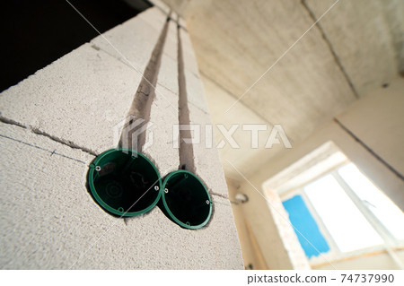 New electrical wiring installation, plastic boxes for electrical cables for future outlet sockets on the wall, renovation concept. New electrical wiring installation, plastic boxes for electrical cables for future outlet sockets on the wall, renovation concept. 74737990