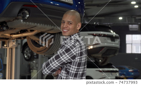 Cheerful African man smiling to the camera standing at cars workshop Cheerful African man smiling to the camera standing at cars workshop 74737993