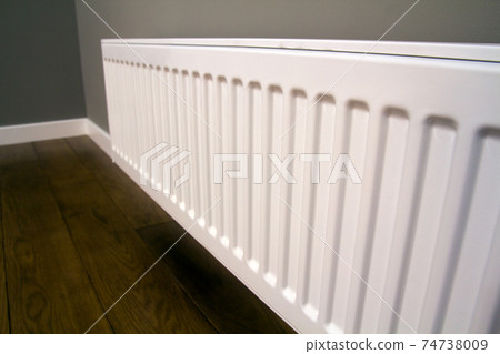 White metal heating radiator mounted on gray wall inside a room. White metal heating radiator mounted on gray wall inside a room. 74738009