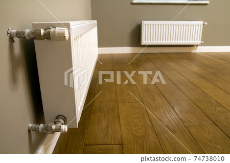 White metal heating radiator mounted on gray wall inside a room. White metal heating radiator mounted on gray wall inside a room. 74738010