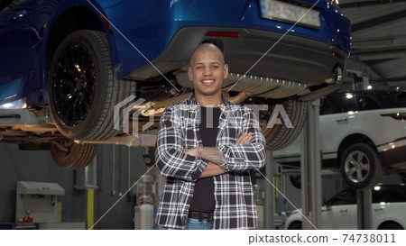 Happy handsome car repairman smiling to the camera at his garage Happy handsome car repairman smiling to the camera at his garage 74738011