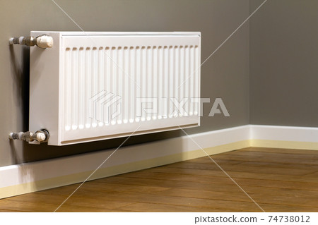 White metal heating radiator mounted on gray wall inside a room. 74738012
