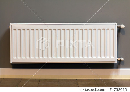 White metal heating radiator mounted on gray wall inside a room. White metal heating radiator mounted on gray wall inside a room. 74738013