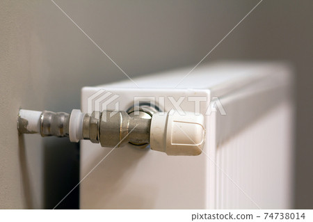 White metal heating radiator mounted on gray wall inside a room. White metal heating radiator mounted on gray wall inside a room. 74738014