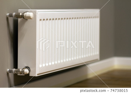 White metal heating radiator mounted on gray wall inside a room. White metal heating radiator mounted on gray wall inside a room. 74738015