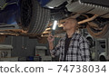 Handsome man examining lifted car with a lamp at the workshop 74738034