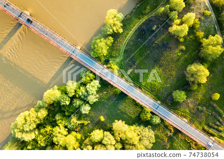 Aerial view of a narrow road bridge stretching over muddy wide river in green rural area. 74738054
