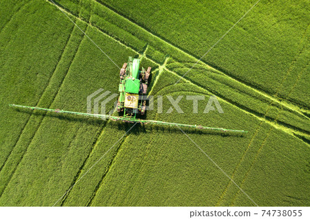 Tractor spraying chemical pesticides with sprayer on the large green agricultural field at spring. 74738055