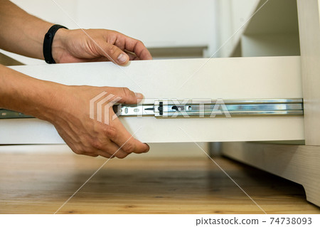 Close up of carpenter hands installing wooden drawer on sliding skids in contemporary cupboard cabinet. Close up of carpenter hands installing wooden drawer on sliding skids in contemporary cupboard cabinet. 74738093