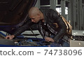 Young African man examining engine of his car at the garage 74738096