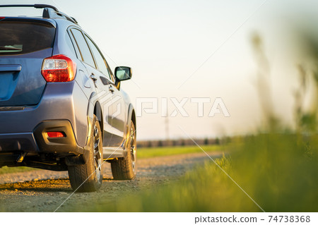 Landscape with blue off road car on gravel road. Traveling by auto, adventure in wildlife, expedition or extreme travel on a SUV automobile. Offroad 4x4 vehicle in field at sunrise. 74738368