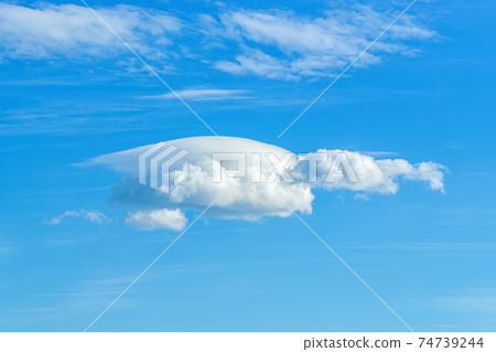 Small lenticular cloud against translucent cirrus clouds high in a clear blue sky. Small lenticular cloud against translucent cirrus clouds high in a clear blue sky. 74739244