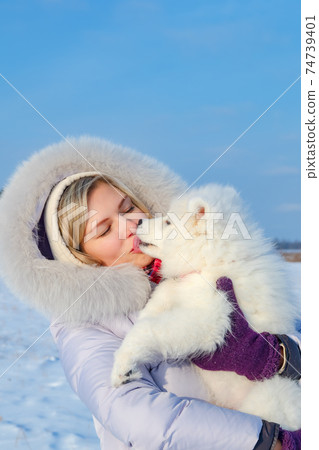 Laughing young woman and samoyed puppy kiss on winter frosty day Laughing young woman and samoyed puppy kiss on winter frosty day 74739401