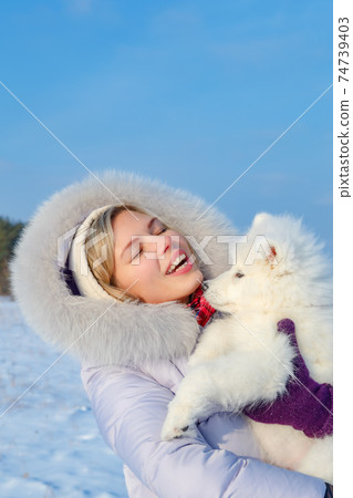 Laughing young woman and samoyed puppy kiss on winter frosty day Laughing young woman and samoyed puppy kiss on winter frosty day 74739403