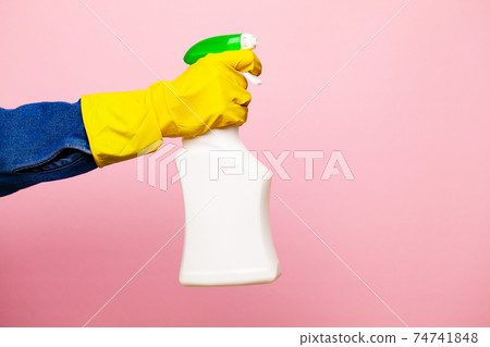 A hand in a yellow glove holds a spray of cleaning fluid on a pink background. A hand in a yellow glove holds a spray of cleaning fluid on a pink background. 74741848