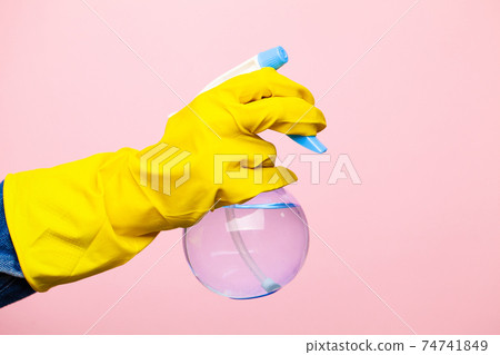 A hand in a yellow glove holds a spray of cleaning fluid on a pink background. A hand in a yellow glove holds a spray of cleaning fluid on a pink background. 74741849