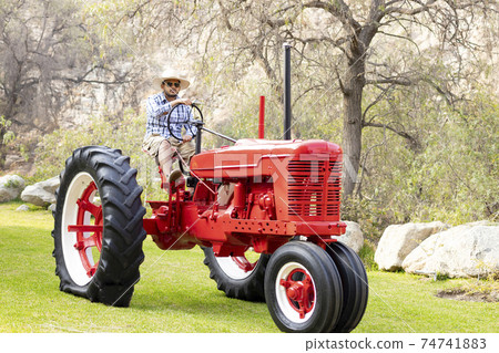 Handsome man with sunglasses driving the tractor to work on the farm Handsome man with sunglasses driving the tractor to work on the farm 74741883