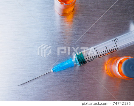 Syringe and ampoules with orange coronavirus vaccine on a aluminum background.  74742185