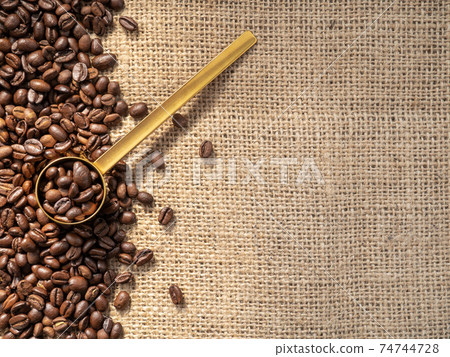 Coffee beans and golden measuring spoon on canvas Coffee beans and golden measuring spoon on canvas 74744728