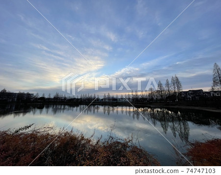 Blue sky peeking through the clouds above the pond Blue sky peeking through the clouds above the pond 74747103