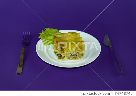 Serving lasagna on a white plate with lettuce. 74748743