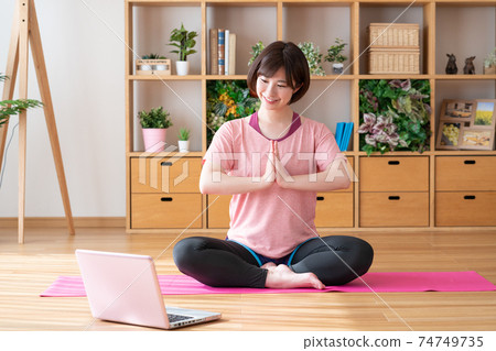 Online yoga A young woman doing a yoga gassho pose while looking at a computer in the living room Online yoga A young woman doing a yoga gassho pose while looking at a computer in the living room 74749735