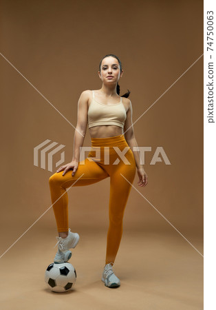 Beautiful young woman with soccer ball standing in studio 74750063