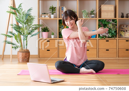 Online yoga young woman stretching in the living room 74750608