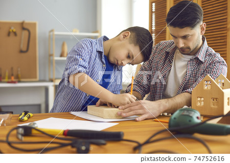 Little boy and his father making wooden house models as part of school DIY project 74752616