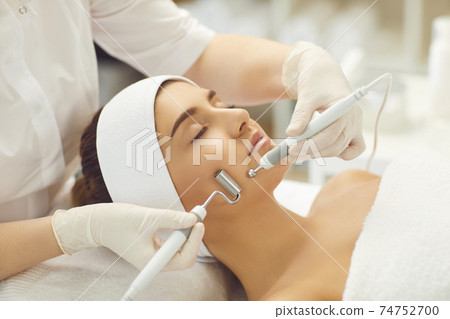 Woman face receiving facial microcurrent treatment with apparatus from therapist Woman face receiving facial microcurrent treatment with apparatus from therapist 74752700