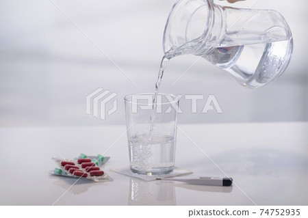 Hand pouring water into a glass next to medication 74752935