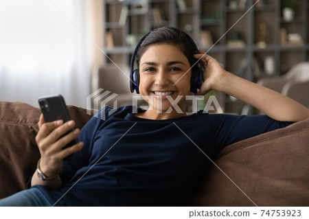 Portrait of happy Indian woman listen to music in headphones 74753923