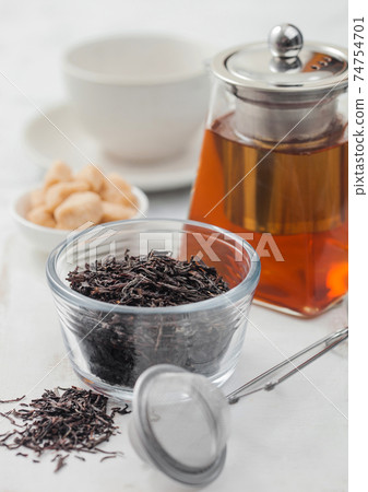 Loose organic black tea with strainer infuser and clear glass teapot with cane sugar  74754701