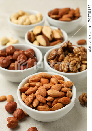 Bowls with different nuts on white textured background, space for text 74758323
