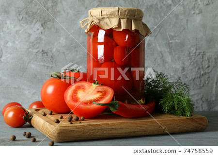 Board with jar of pickled tomatoes on wooden table 74758559