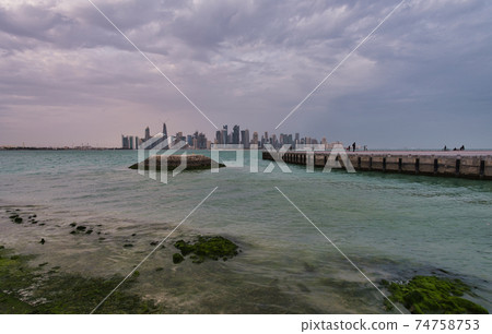 Doha skyline from the corniche promenade afternoon wide angle shot showing dhows with Qatar flag in the Arabic gulf  in foreground and clouds in the sky in background 74758753