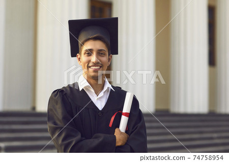 Smiling boy university graduate standing and holding diploma in hand Smiling boy university graduate standing and holding diploma in hand 74758954