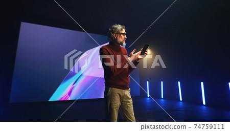 Middle aged speaker explaining smartphone features Middle aged speaker explaining smartphone features 74759111