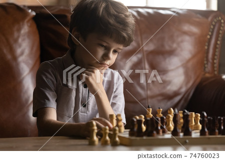 Close up thoughtful little boy playing chess, touching chin 74760023