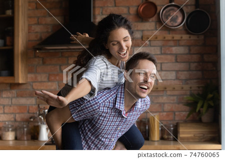 Overjoyed husband piggy backing wife pretending flying, family having fun 74760065