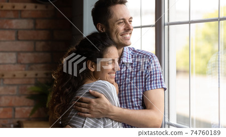 Close up smiling dreamy young couple hugging, visualizing future 74760189
