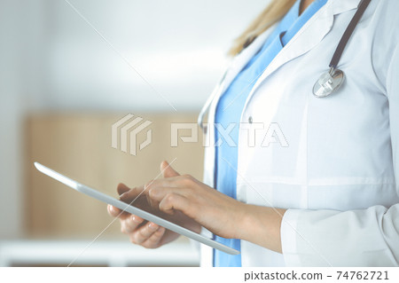 Unknown woman-doctor standing in clinic and using tablet pc, close-up. Data in medicine and healthcare 74762721