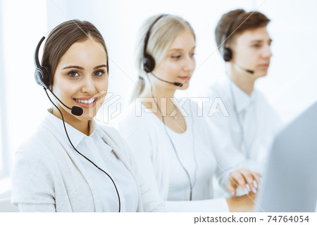 Call center. Group of diverse operators at work. Beautiful woman in headset communicating with customers of telemarketing service. Business concept 74764054