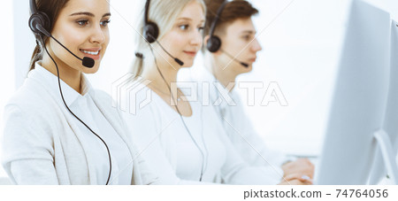 Call center. Group of diverse operators at work. Beautiful woman in headset communicating with customers of telemarketing service. Business concept 74764056