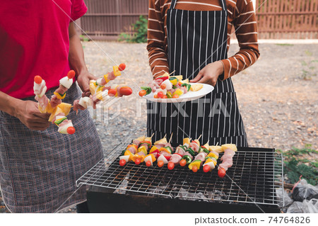 A woman with a barbecue plate and a man grilling barbecue and pork in dinner party. Food, people and family time concept. 74764826