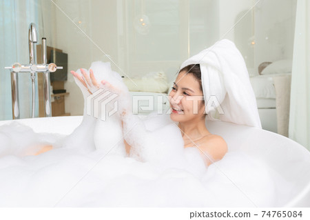 Happy asian woman bathes with white foam in a bathtub fun emotions. 74765084